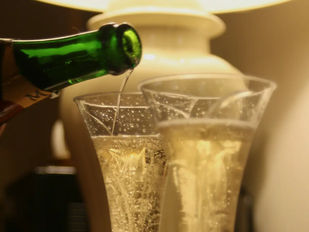 Champagne being poured into two flutes on a bar, the lounge photo behind every page